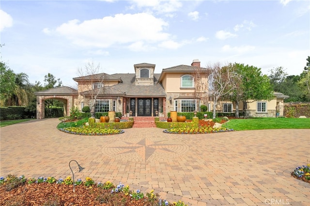 view of front of home with stucco siding, a front lawn, stone siding, curved driveway, and a chimney