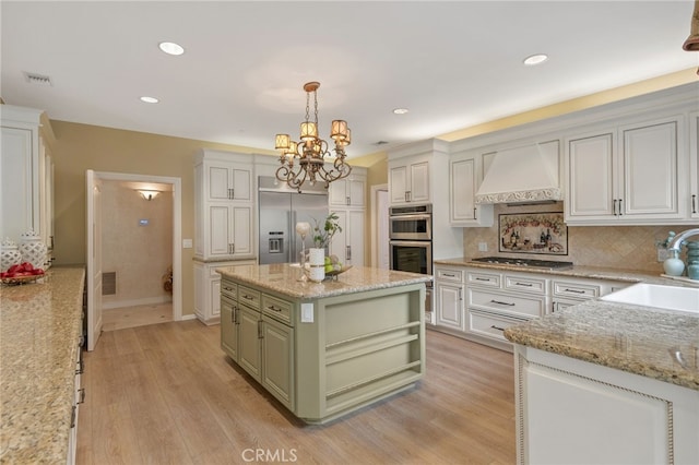 kitchen featuring decorative backsplash, appliances with stainless steel finishes, custom exhaust hood, a notable chandelier, and a sink