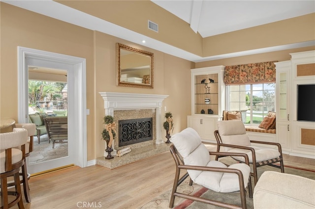 sitting room with a high end fireplace, visible vents, lofted ceiling, and light wood-style floors