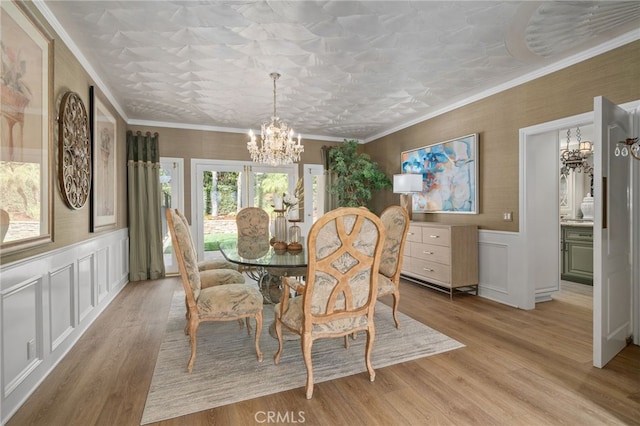 dining room with a wainscoted wall, light wood finished floors, ornamental molding, a decorative wall, and a notable chandelier