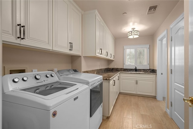 clothes washing area featuring visible vents, independent washer and dryer, a sink, cabinet space, and light wood-style floors