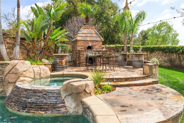 view of patio featuring an in ground hot tub, an outdoor fireplace, fence, and outdoor dry bar