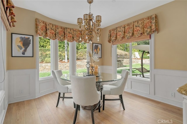 dining space with wainscoting, a notable chandelier, and light wood-style flooring