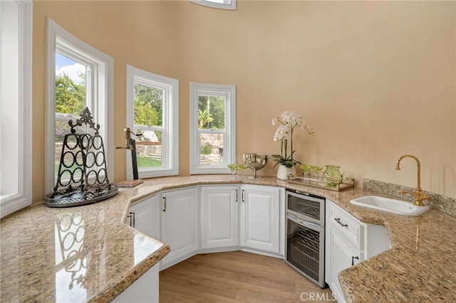 kitchen featuring light wood-type flooring, a sink, light stone counters, white cabinetry, and wine cooler