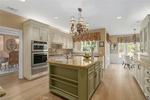 kitchen featuring custom range hood, green cabinets, double oven, a warming drawer, and a chandelier