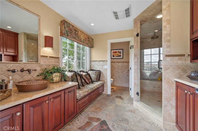 bathroom with visible vents, toilet, a stall shower, stone finish floor, and tile walls