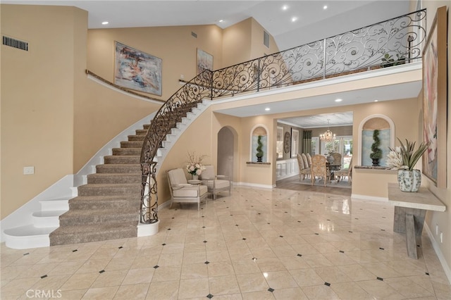 entrance foyer with visible vents, stairway, a high ceiling, an inviting chandelier, and baseboards