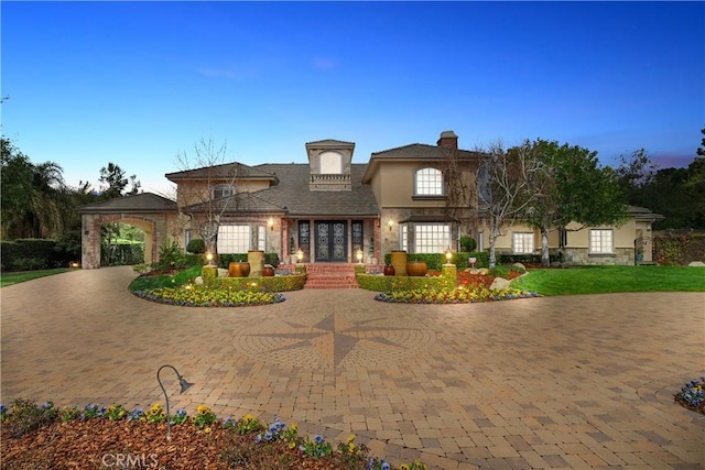 view of front facade with a front yard, stucco siding, a chimney, curved driveway, and stone siding