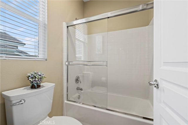 bathroom featuring toilet and shower / bath combination with glass door