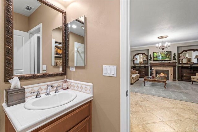 bathroom featuring vanity, visible vents, an inviting chandelier, a lit fireplace, and crown molding