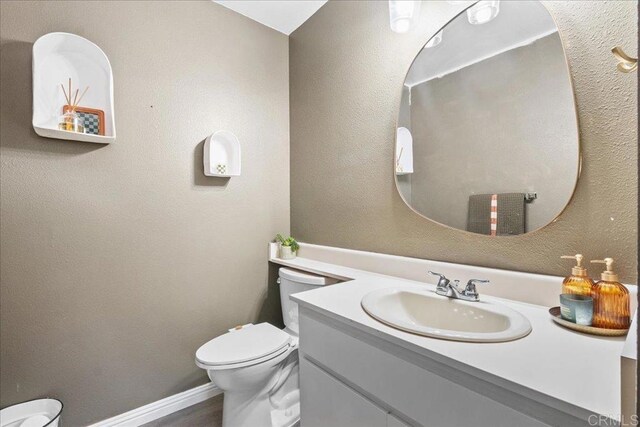 half bath with toilet, vanity, baseboards, and a textured wall