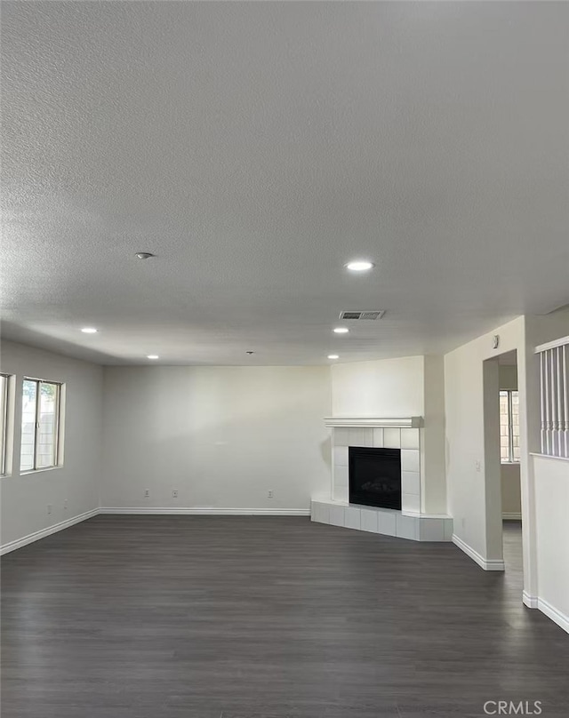 unfurnished living room with visible vents, baseboards, dark wood-type flooring, and a tile fireplace