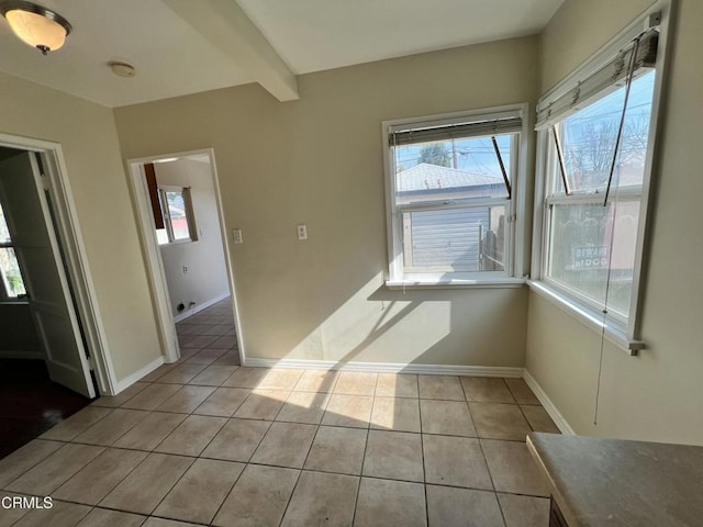 empty room with light tile patterned floors, beam ceiling, baseboards, and a wealth of natural light