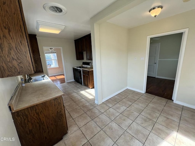 kitchen with dark brown cabinets, light countertops, gas range oven, light tile patterned floors, and a sink