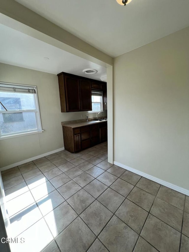 kitchen featuring light tile patterned floors, baseboards, plenty of natural light, and dark brown cabinetry