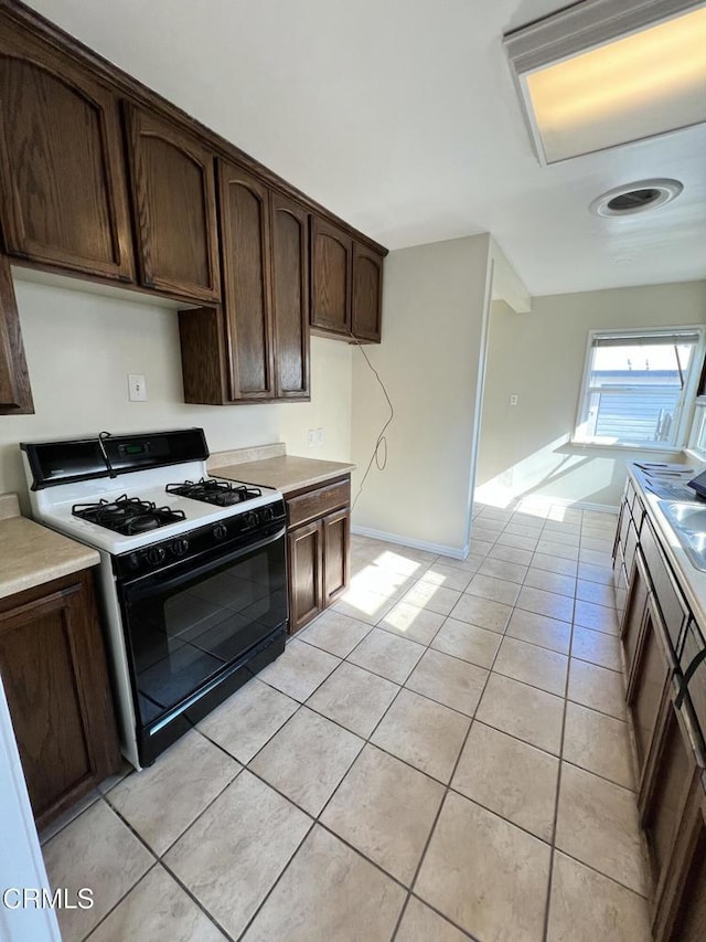 kitchen featuring dark brown cabinetry, light tile patterned floors, light countertops, and gas range oven