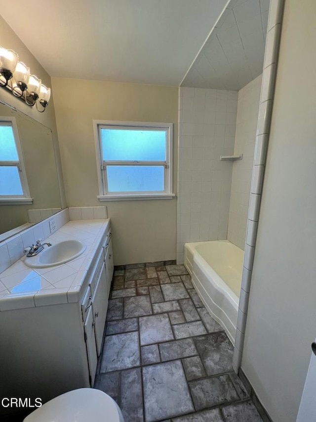 full bath with vanity, toilet, a healthy amount of sunlight, and stone finish flooring