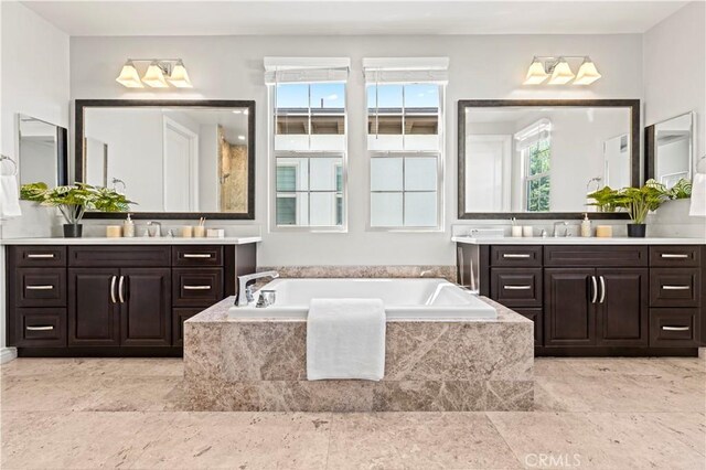 bathroom featuring a garden tub, two vanities, and a sink