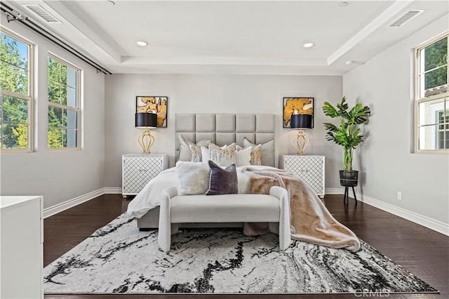 bedroom featuring a tray ceiling, visible vents, baseboards, and dark wood-style flooring