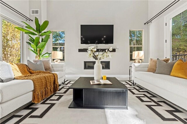 living room featuring visible vents, baseboards, a glass covered fireplace, and a towering ceiling