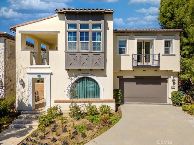 view of front of house with a tiled roof, stucco siding, a garage, a balcony, and driveway