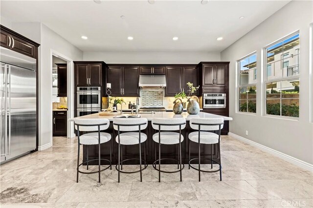 kitchen featuring backsplash, under cabinet range hood, a kitchen bar, light countertops, and stainless steel appliances