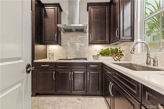 kitchen featuring gas cooktop, a sink, light countertops, dark brown cabinetry, and wall chimney range hood