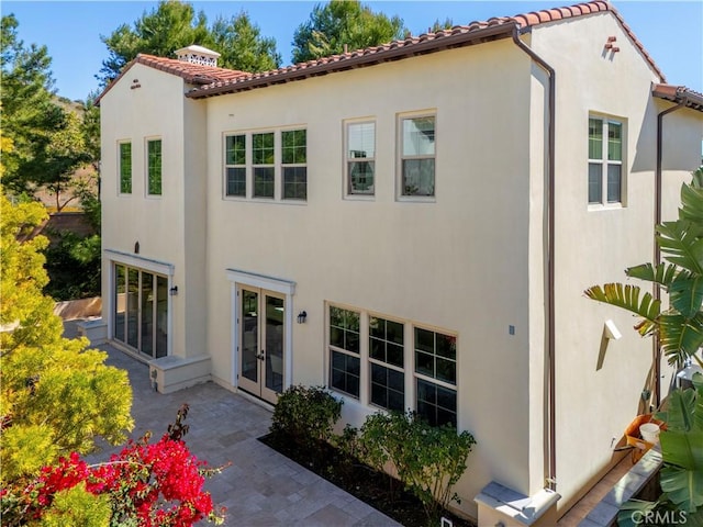 rear view of house with a patio, a tiled roof, french doors, and stucco siding