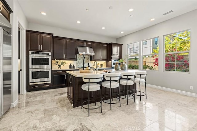 kitchen with visible vents, light countertops, appliances with stainless steel finishes, under cabinet range hood, and a kitchen bar