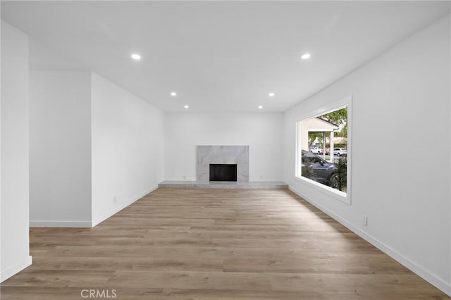 unfurnished living room featuring recessed lighting, a fireplace, baseboards, and light wood finished floors