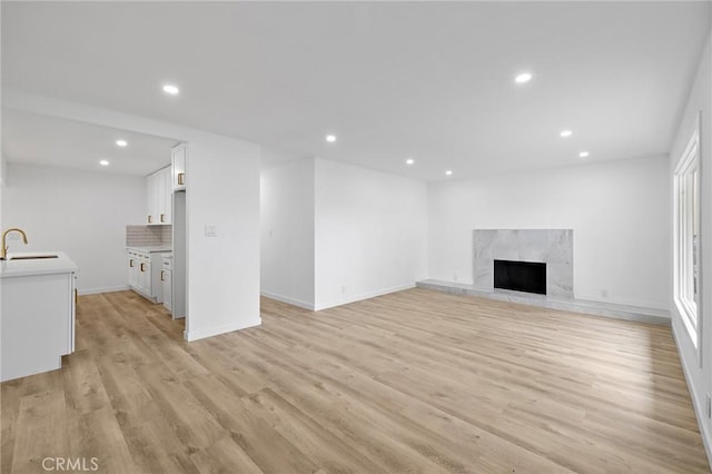 unfurnished living room featuring a premium fireplace, recessed lighting, light wood-style floors, and a sink