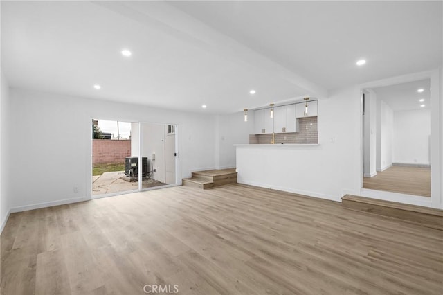 unfurnished living room featuring a wood stove, recessed lighting, light wood-style floors, and baseboards