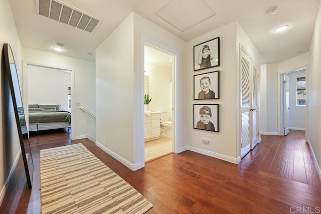 hall featuring visible vents, attic access, baseboards, and dark wood-style flooring