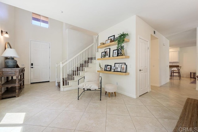 stairway with tile patterned floors, visible vents, baseboards, and a high ceiling