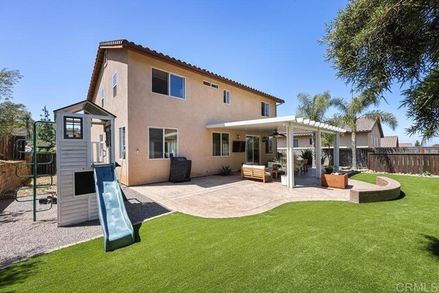 rear view of house featuring stucco siding, a lawn, a playground, fence, and a patio area