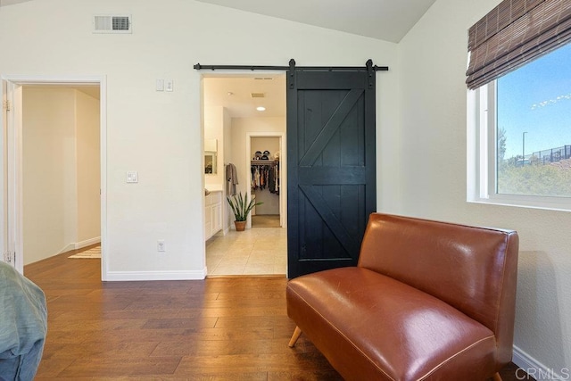 sitting room with visible vents, lofted ceiling, wood finished floors, a barn door, and baseboards