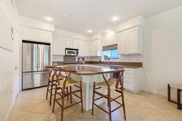 kitchen with light tile patterned floors, stainless steel appliances, white cabinets, a kitchen bar, and backsplash