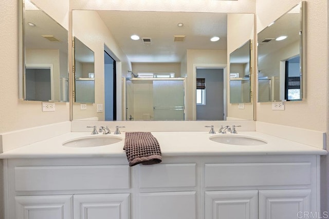 full bathroom with double vanity, visible vents, a shower stall, and a sink