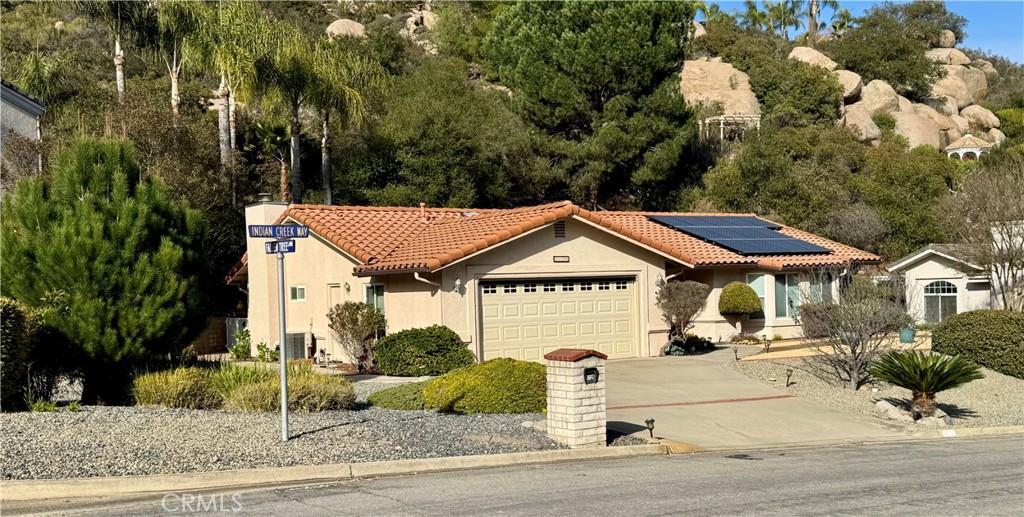 mediterranean / spanish home with solar panels, a tiled roof, stucco siding, a garage, and driveway