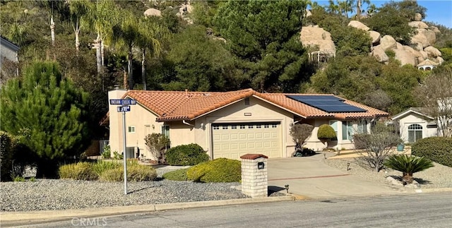 mediterranean / spanish home with solar panels, a tiled roof, stucco siding, a garage, and driveway