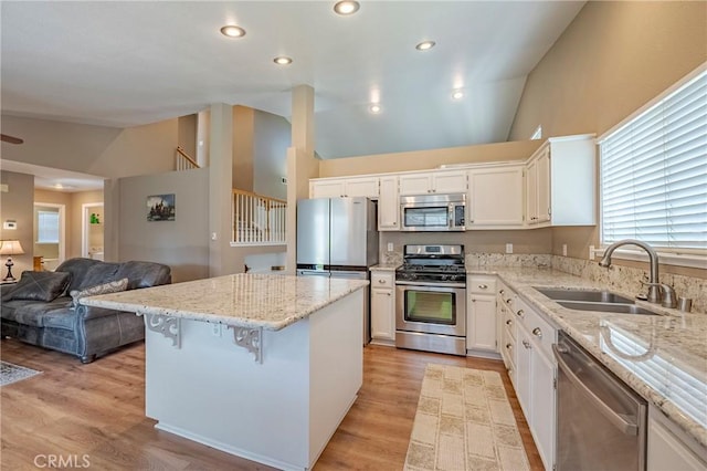 kitchen featuring a sink, a center island, stainless steel appliances, light stone countertops, and vaulted ceiling