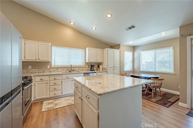 kitchen with visible vents, a kitchen island, lofted ceiling, appliances with stainless steel finishes, and a sink