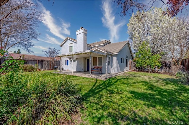 back of house with a fenced backyard, a lawn, a chimney, and a patio