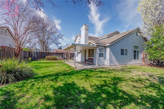 rear view of house featuring stucco siding, a fenced backyard, a yard, a chimney, and a patio area