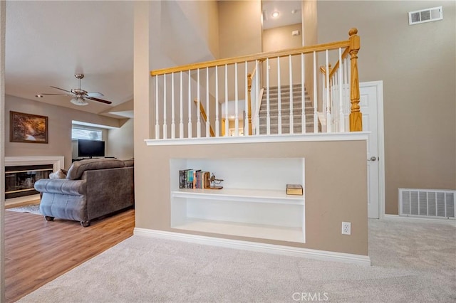 stairs with visible vents, carpet floors, a ceiling fan, and a glass covered fireplace