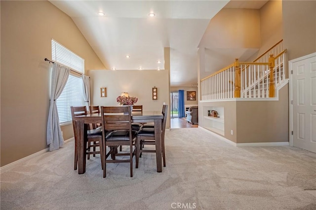 carpeted dining area with baseboards, high vaulted ceiling, and stairs