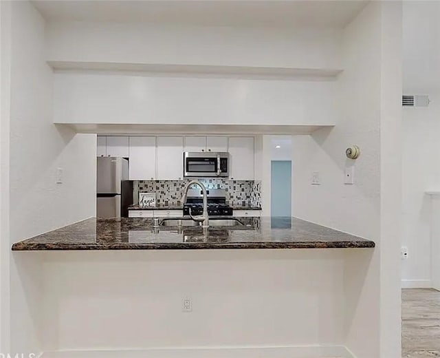 kitchen featuring backsplash, a peninsula, white cabinets, stainless steel appliances, and a sink