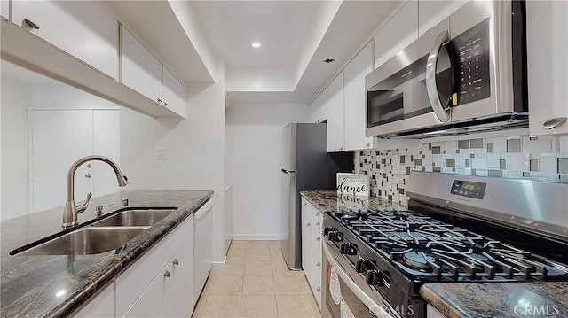 kitchen featuring dark stone countertops, a sink, stainless steel appliances, white cabinetry, and backsplash