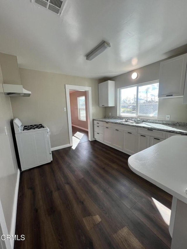 kitchen featuring baseboards, washer / dryer, dark wood-style floors, white cabinetry, and a sink