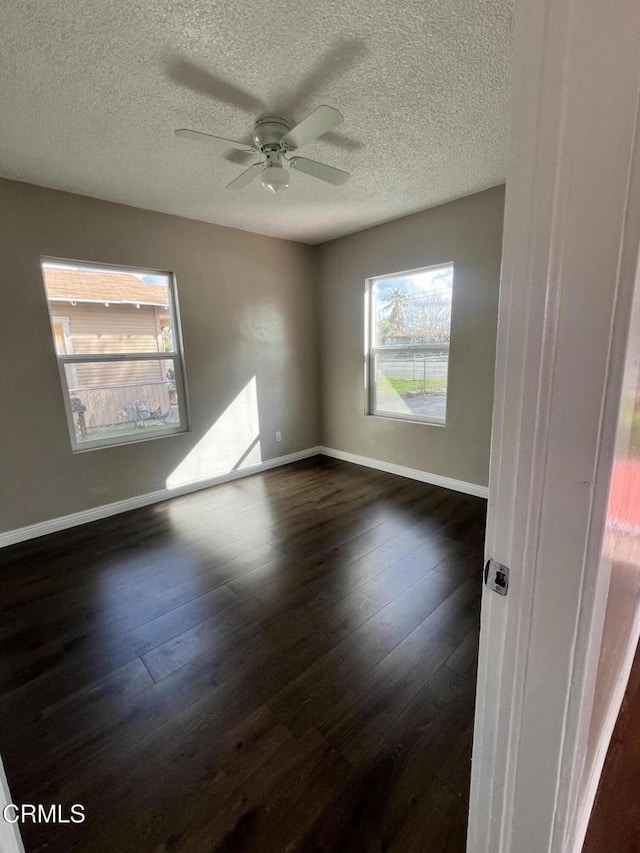 empty room with baseboards, a textured ceiling, dark wood finished floors, and a ceiling fan